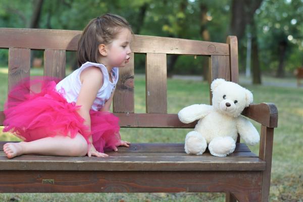 Mädchen betrachtet einen Teddybären auf einer Bank